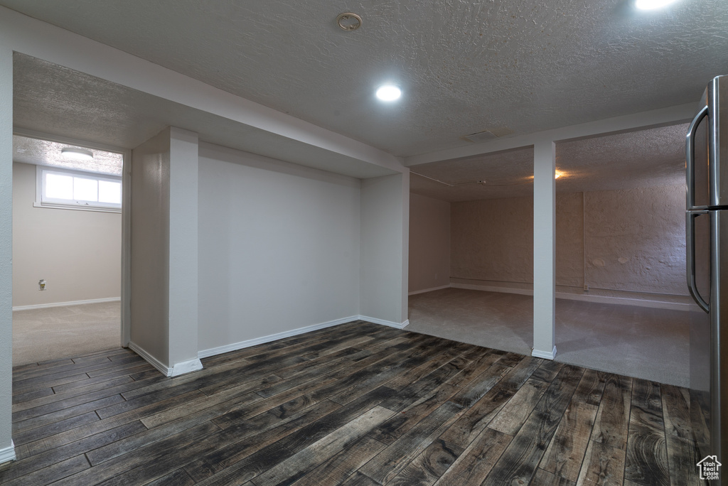 Below grade area featuring dark wood finished floors, freestanding refrigerator, and a textured ceiling