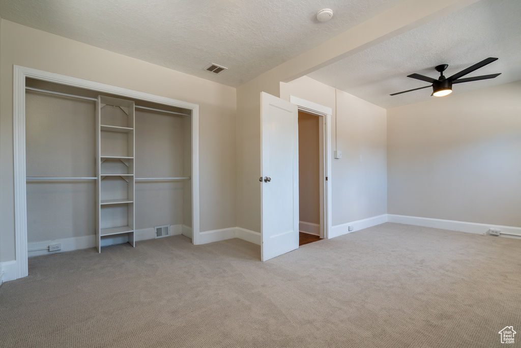 Unfurnished bedroom with carpet floors, a closet, a textured ceiling, and a ceiling fan