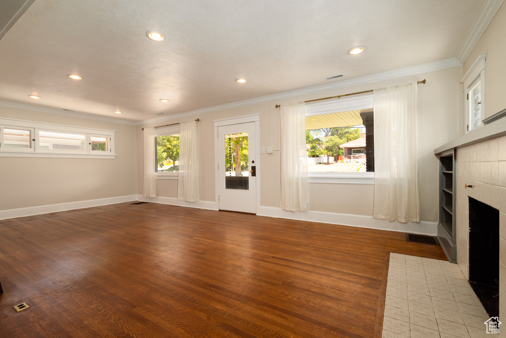 Unfurnished living room with a tile fireplace, wood finished floors, ornamental molding, and recessed lighting