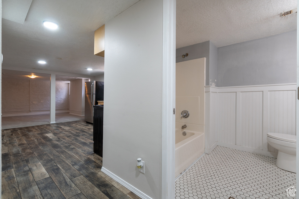Full bathroom featuring a decorative wall, wood finished floors, wainscoting, washtub / shower combination, and a textured ceiling