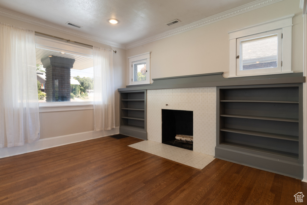 Unfurnished living room with wood finished floors, crown molding, a tile fireplace, recessed lighting, and built in features