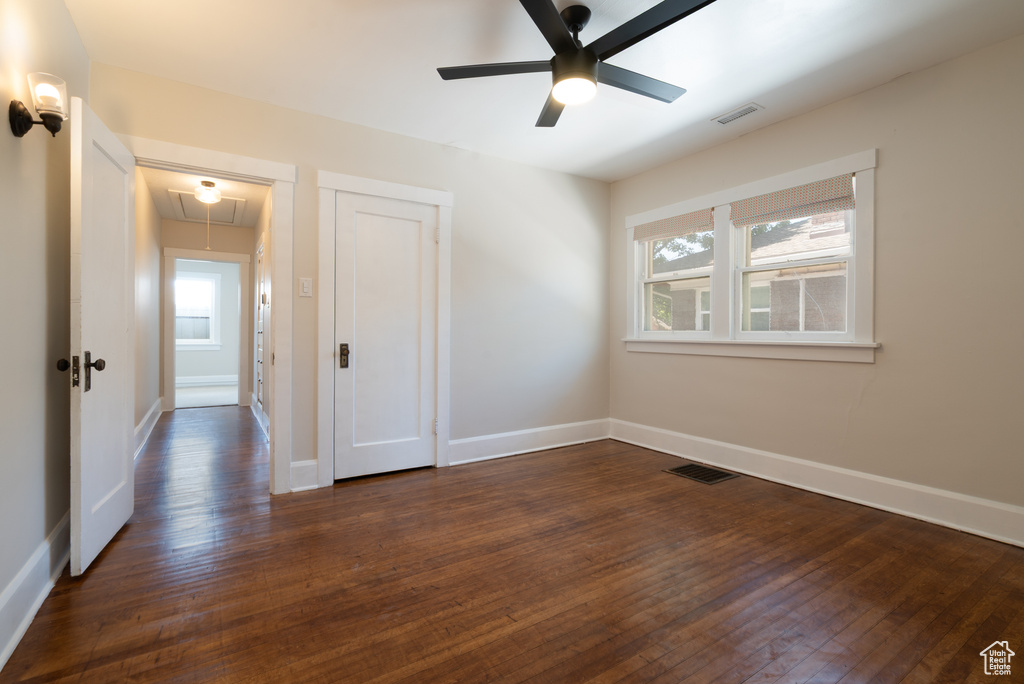 Unfurnished bedroom with attic access, dark wood-style flooring, and multiple windows