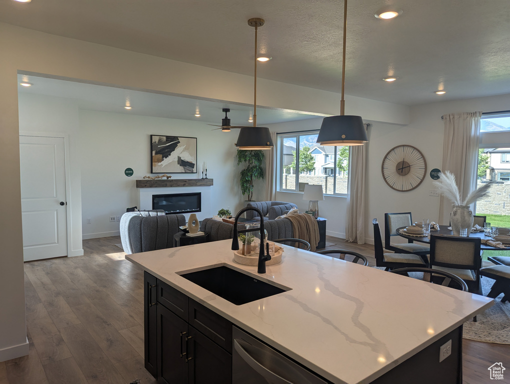 Kitchen featuring open floor plan, dishwasher, a ceiling fan, a glass covered fireplace, and light stone countertops