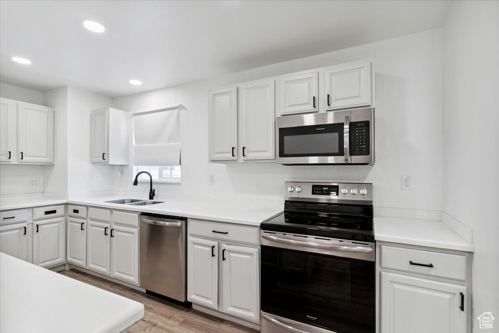 Kitchen with appliances with stainless steel finishes, light wood-style floors, white cabinets, recessed lighting, and light countertops