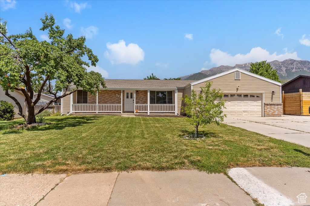 Single story home featuring brick siding, covered porch, driveway, a garage, and a front yard