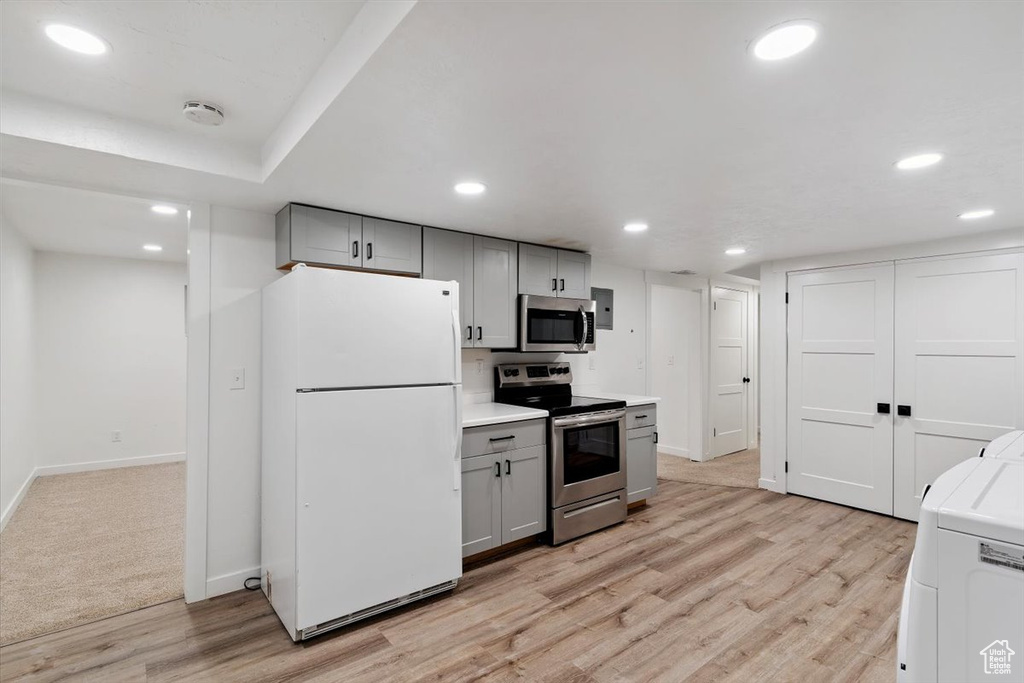 Kitchen with appliances with stainless steel finishes, gray cabinetry, washer / clothes dryer, light wood-style floors, and light countertops