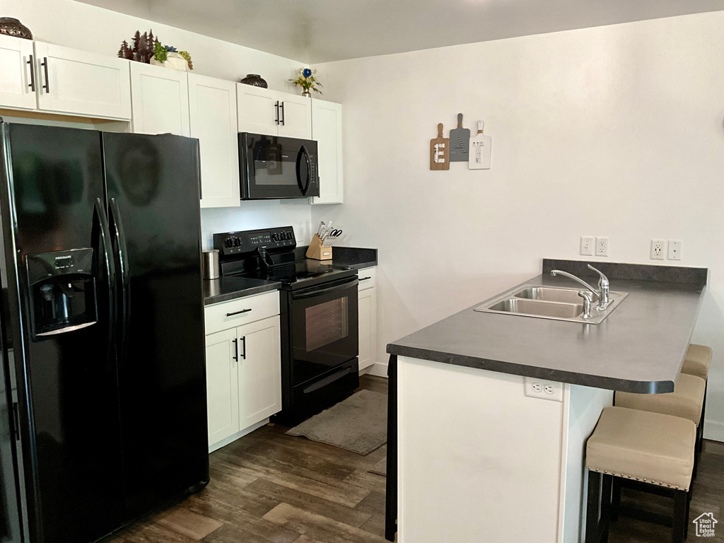 Kitchen with black appliances, a peninsula, a kitchen bar, dark wood-style flooring, and dark countertops