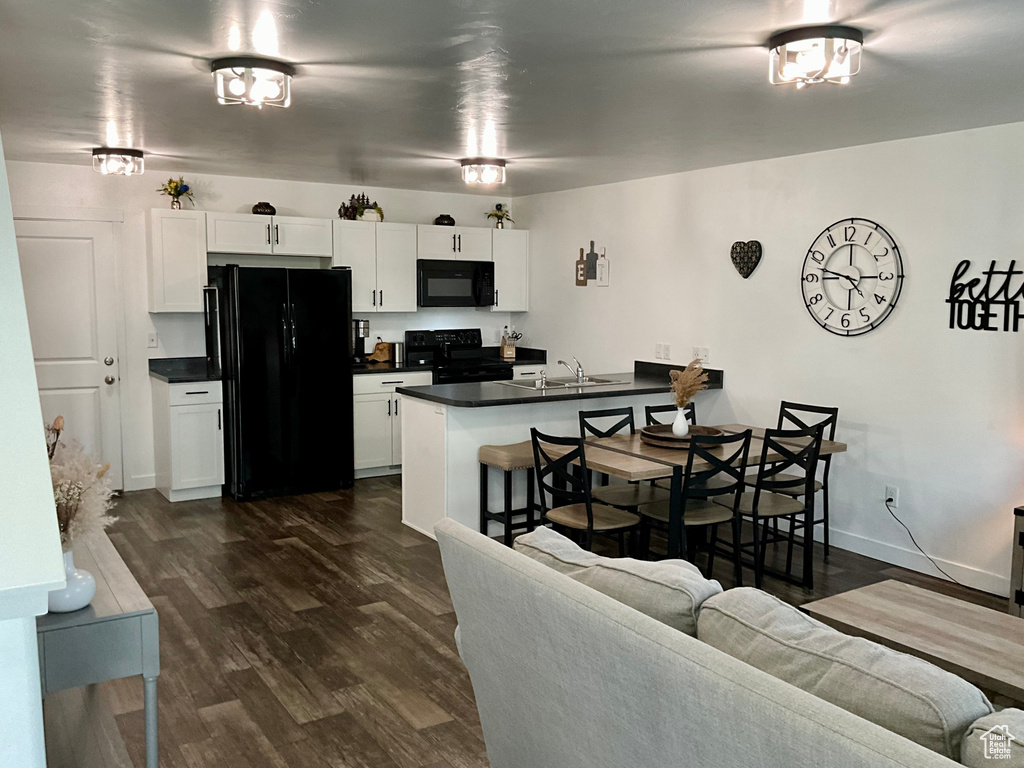 Kitchen featuring black appliances, dark countertops, a peninsula, a kitchen breakfast bar, and dark wood-style floors