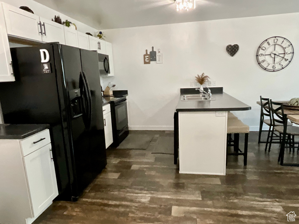 Kitchen featuring black appliances, a breakfast bar, dark countertops, and white cabinets