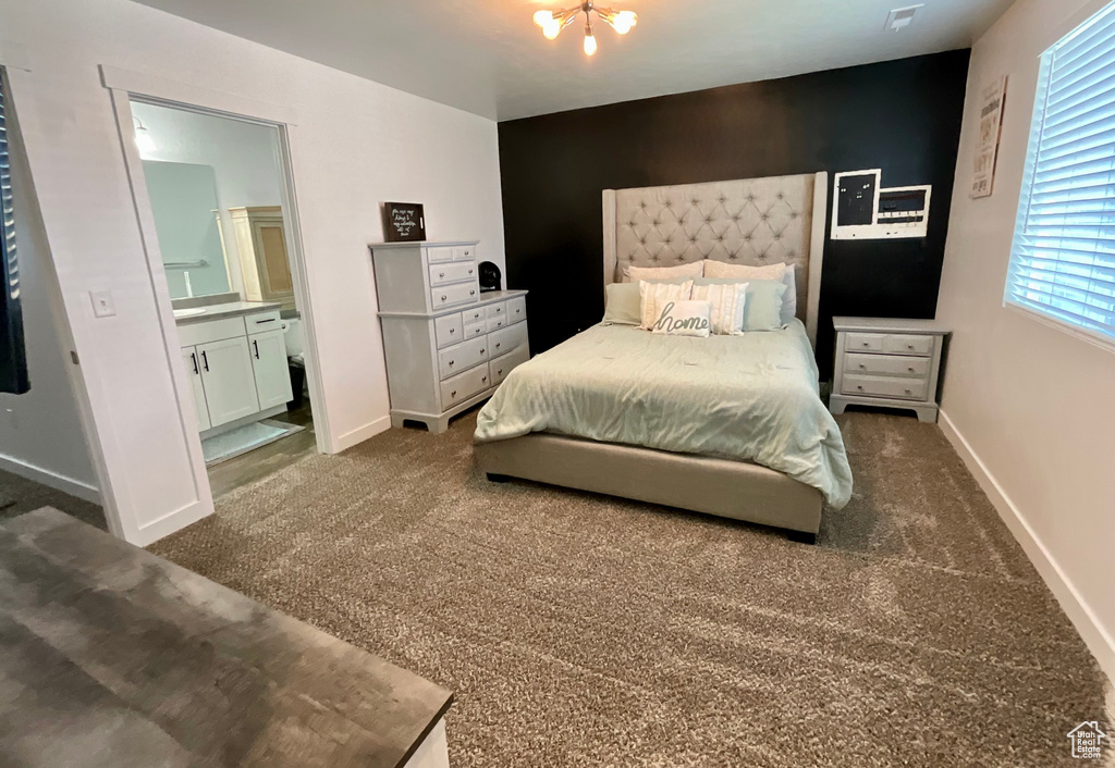 Bedroom featuring dark carpet, ensuite bath, an accent wall, and a chandelier