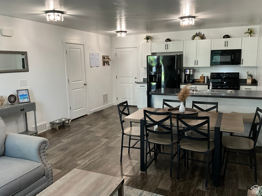 Kitchen featuring black appliances, dark countertops, white cabinetry, and dark wood-type flooring