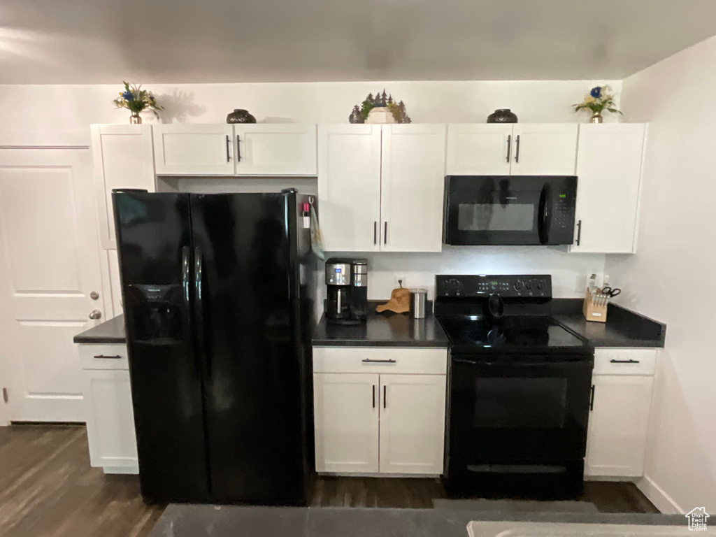 Kitchen with black appliances, dark countertops, and white cabinetry