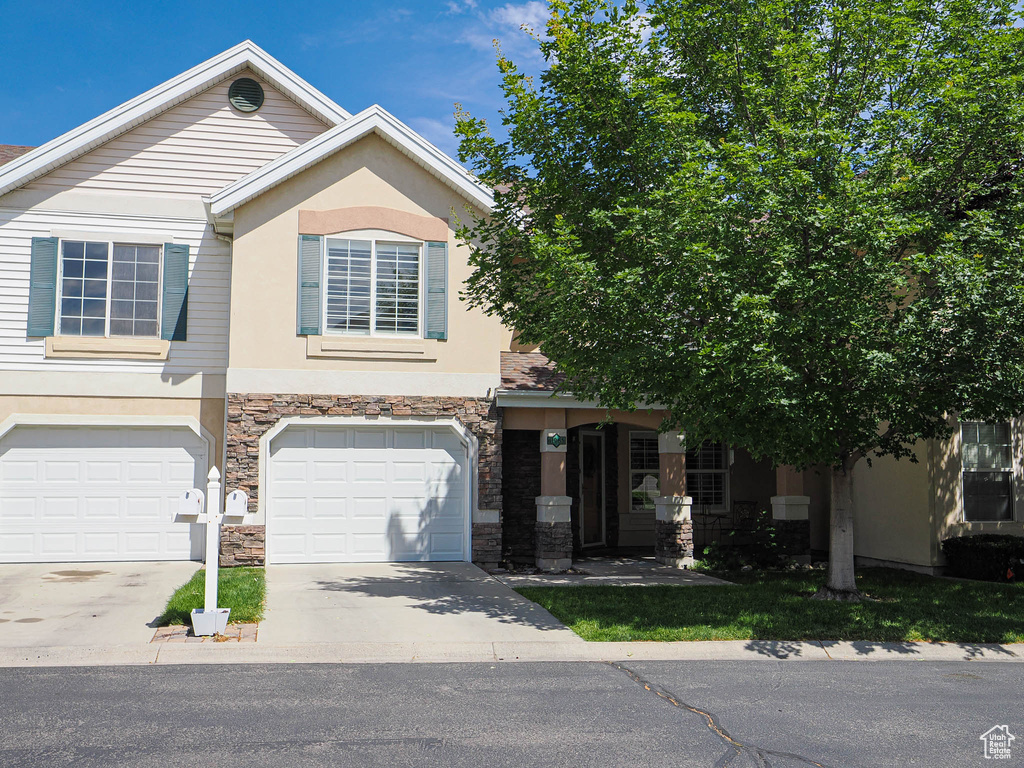 View of front of property featuring stone siding, driveway, stucco siding, and a garage