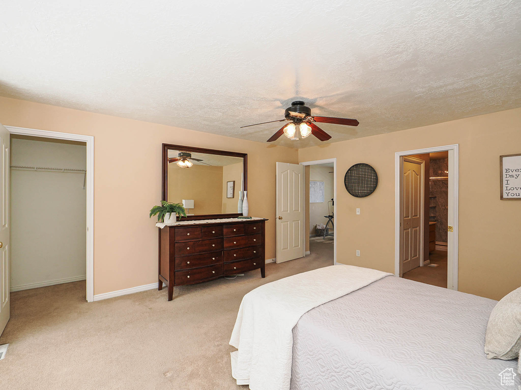 Bedroom with a spacious closet, light carpet, ceiling fan, and ensuite bathroom