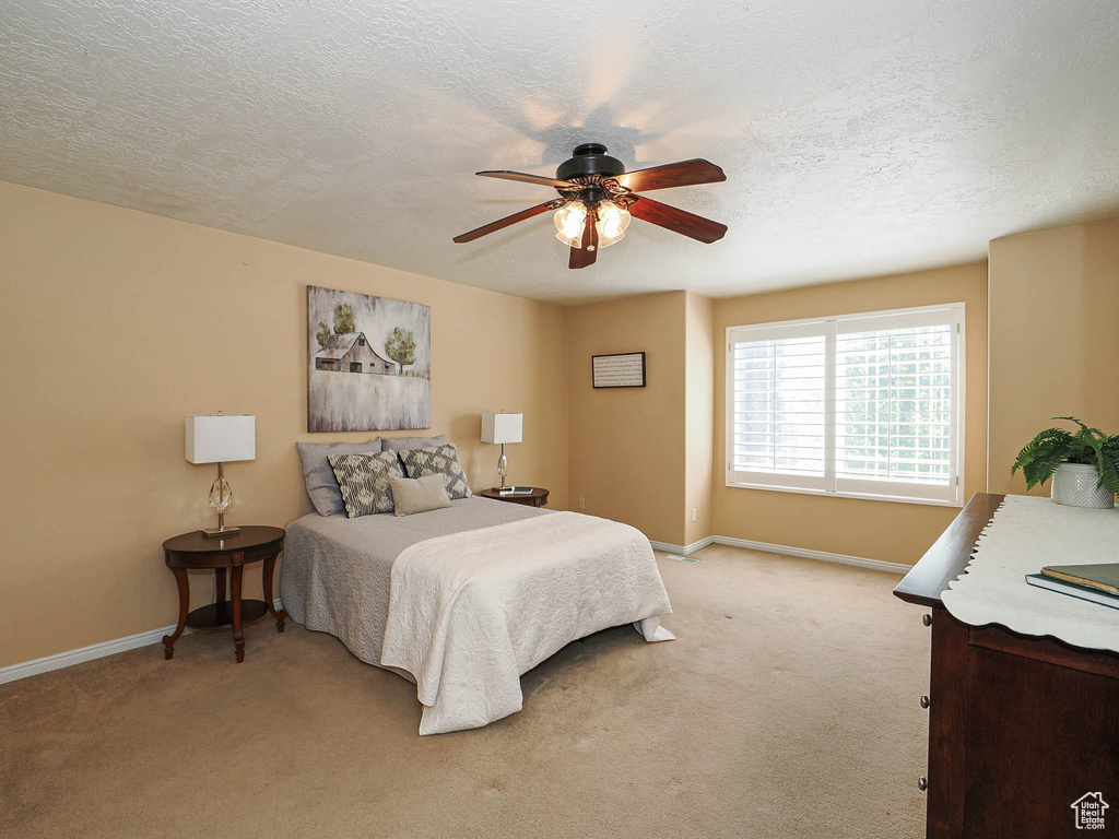 Bedroom with light colored carpet, a textured ceiling, and ceiling fan