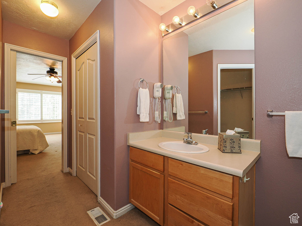 Ensuite bathroom featuring a closet, vanity, a ceiling fan, and a textured ceiling