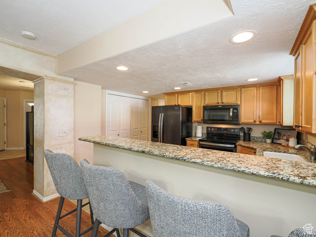 Kitchen with black appliances, a textured ceiling, dark wood-style flooring, recessed lighting, and light stone counters