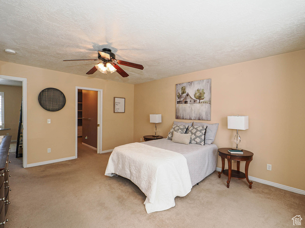 Bedroom with light colored carpet, a textured ceiling, a spacious closet, and a ceiling fan