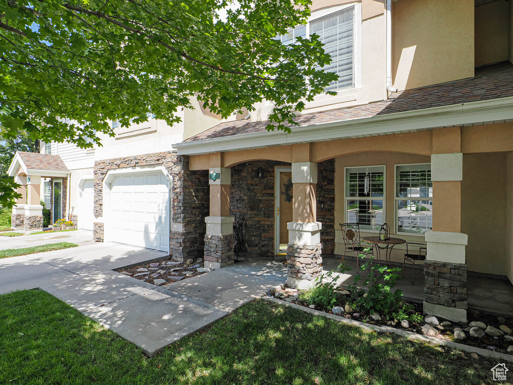 View of front of property featuring covered porch, stucco siding, stone siding, and an attached garage
