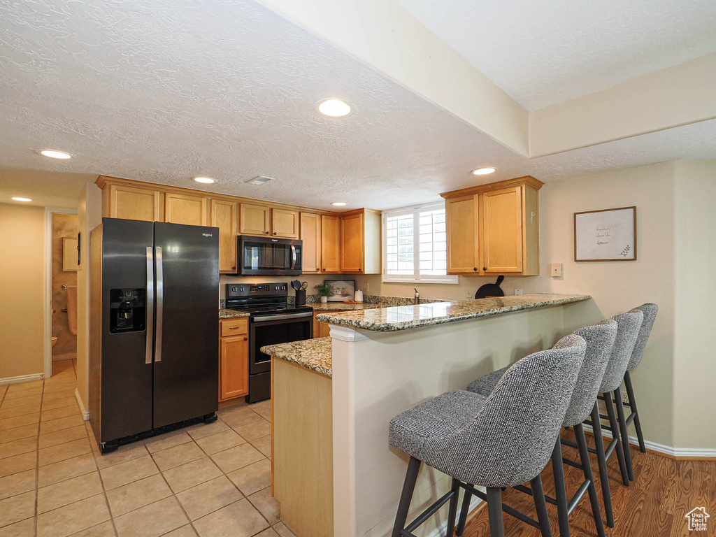 Kitchen featuring stainless steel fridge, black electric range oven, a peninsula, recessed lighting, and light stone countertops