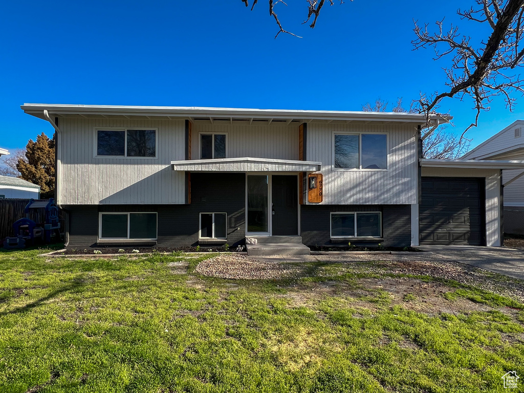 Back of house featuring a lawn, entry steps, an attached garage, and driveway