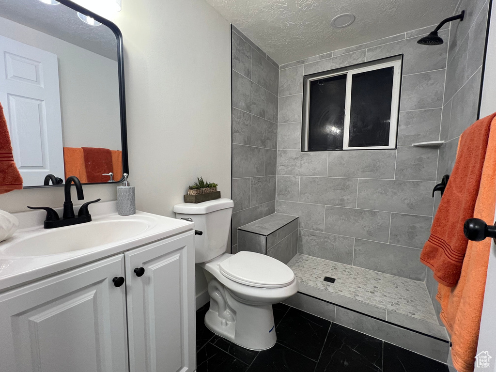 Full bath featuring a tile shower, a textured ceiling, and vanity