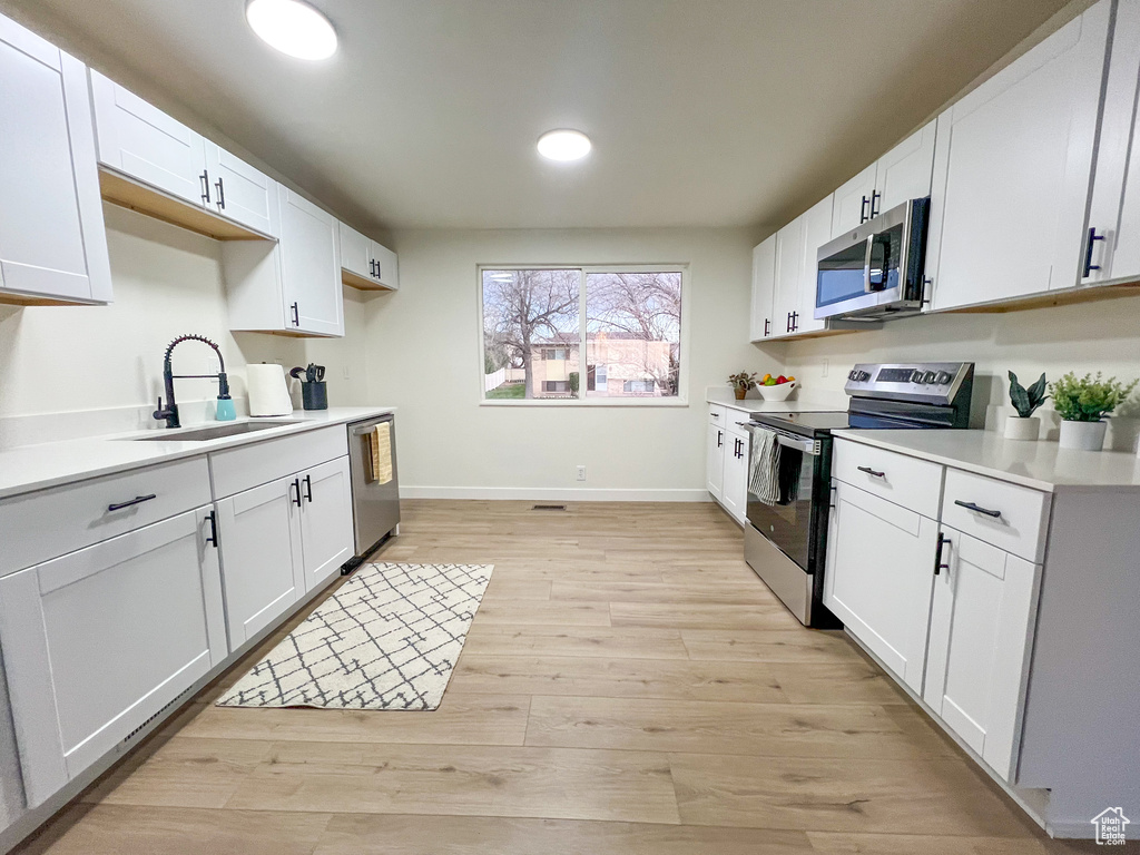 Kitchen featuring appliances with stainless steel finishes, light countertops, light wood-type flooring, white cabinetry, and recessed lighting