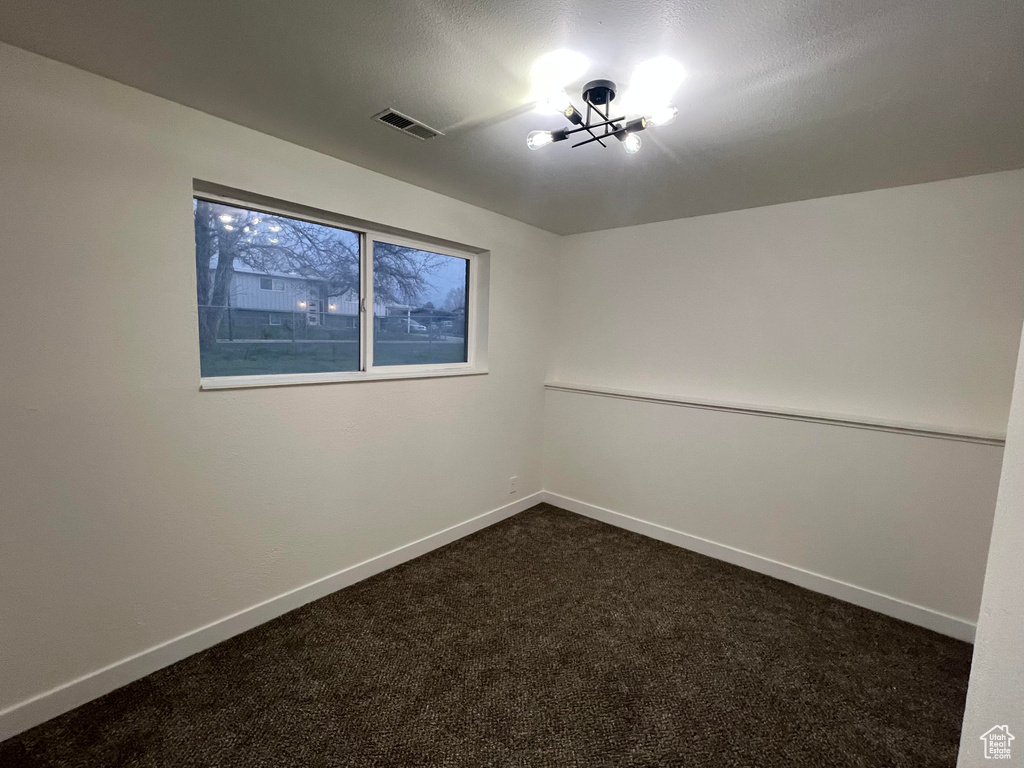 Spare room with dark colored carpet and a chandelier