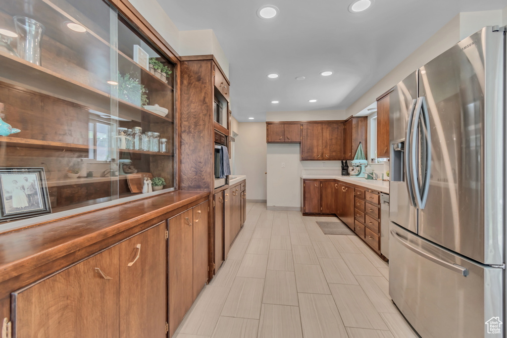 Kitchen featuring stainless steel appliances, recessed lighting, brown cabinetry, open shelves, and glass insert cabinets