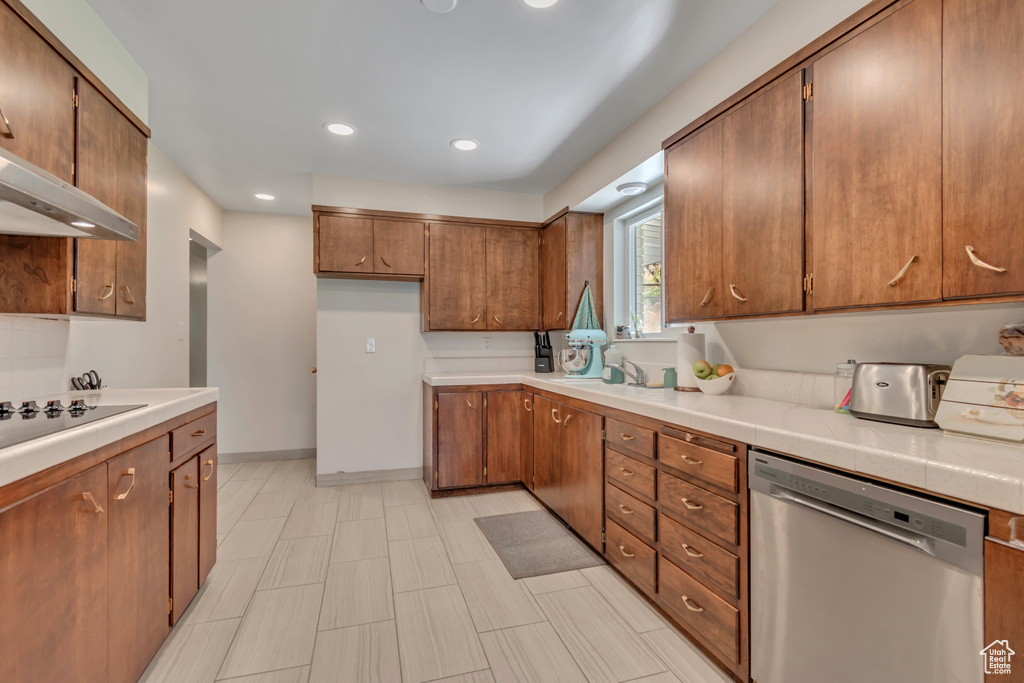 Kitchen featuring stainless steel dishwasher, black electric stovetop, brown cabinetry, wall chimney exhaust hood, and recessed lighting