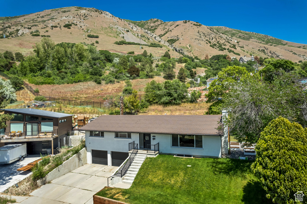 View of front of house featuring a garage, driveway, a mountain view, and a front yard