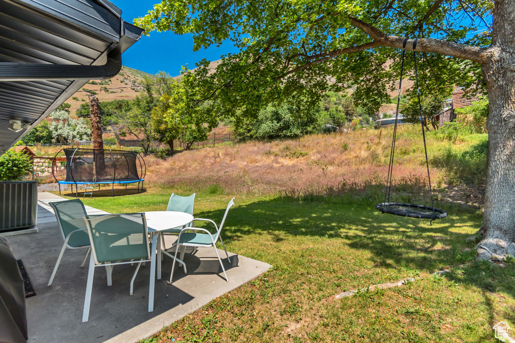 View of grassy yard featuring a trampoline, a patio, and outdoor dining area