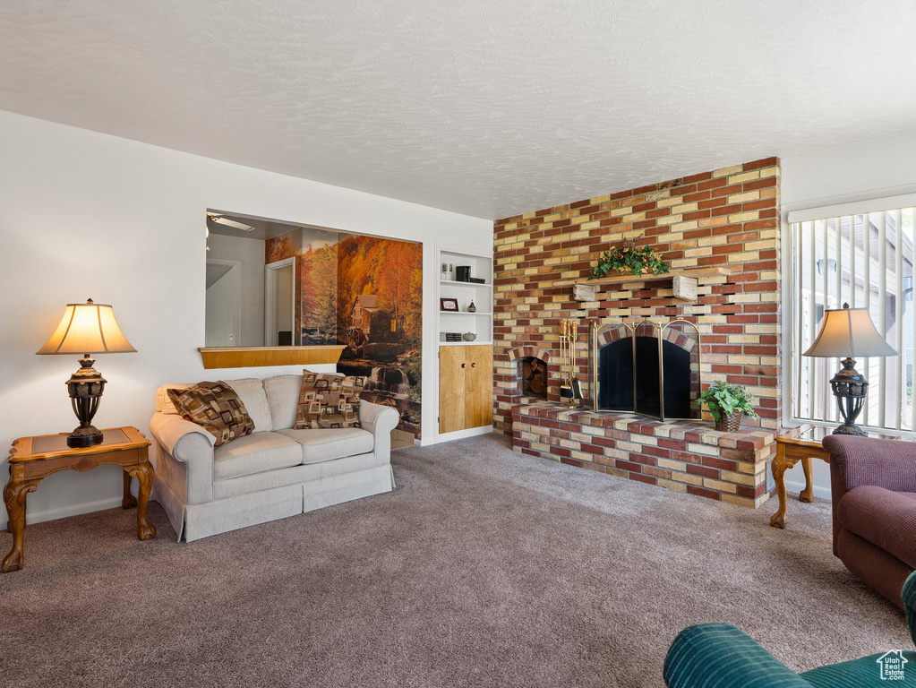 Carpeted living room featuring a brick fireplace, a textured ceiling, and built in shelves