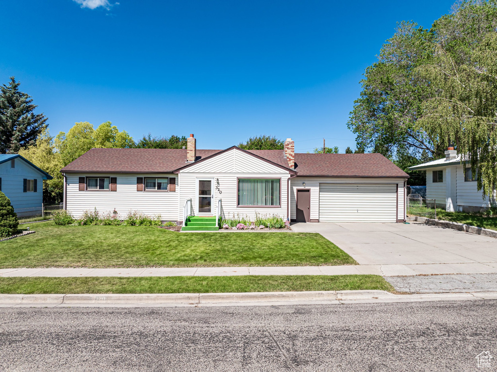 Single story home featuring a garage, driveway, a chimney, and a front lawn