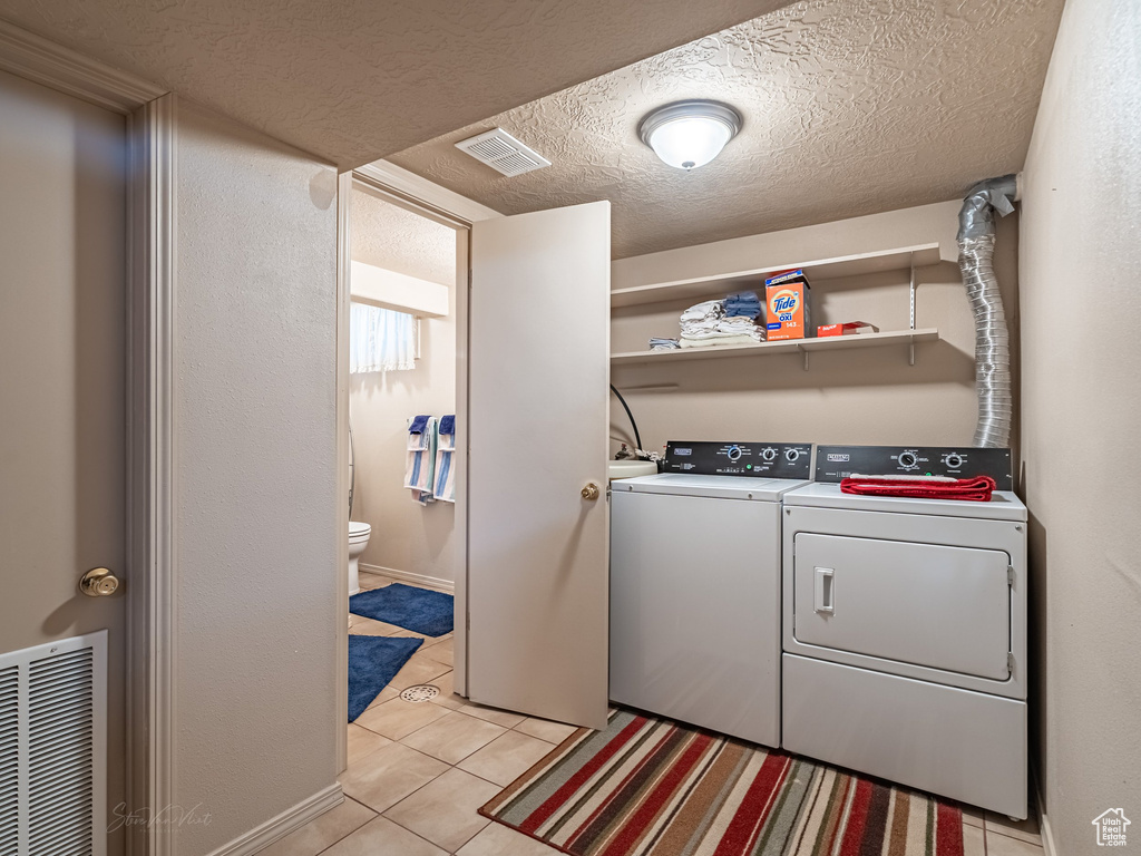 Laundry area featuring washer and dryer, light tile patterned floors, and a textured ceiling