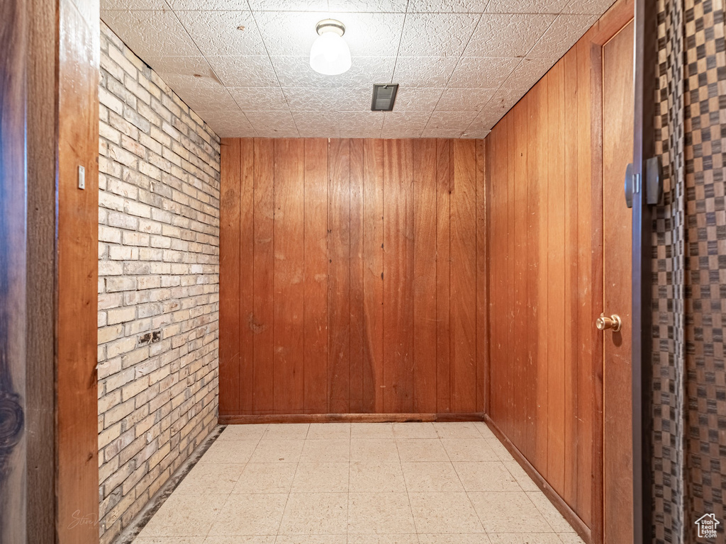 Hallway with light floors, wooden walls, and brick wall