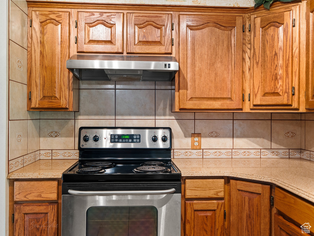 Kitchen with stainless steel electric range oven, under cabinet range hood, backsplash, and brown cabinets
