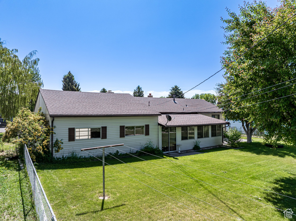 Rear view of property with a yard, roof with shingles, and a sunroom