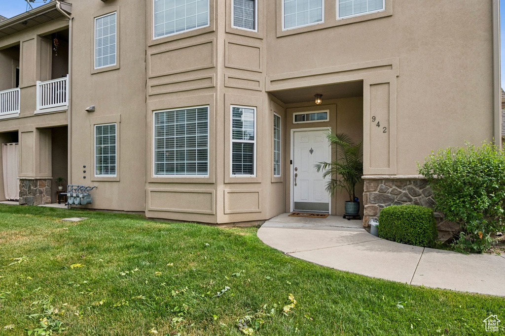 Doorway to property with stucco siding, a lawn, and stone siding