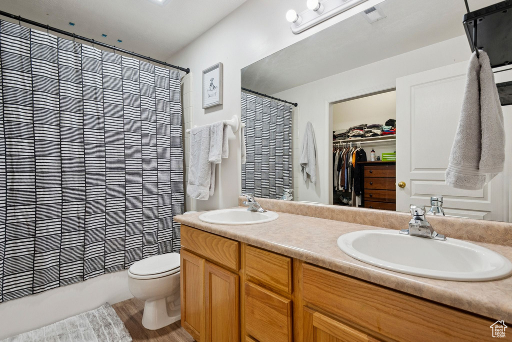Bathroom with double vanity, a spacious closet, shower / bath combo with shower curtain, and wood finished floors