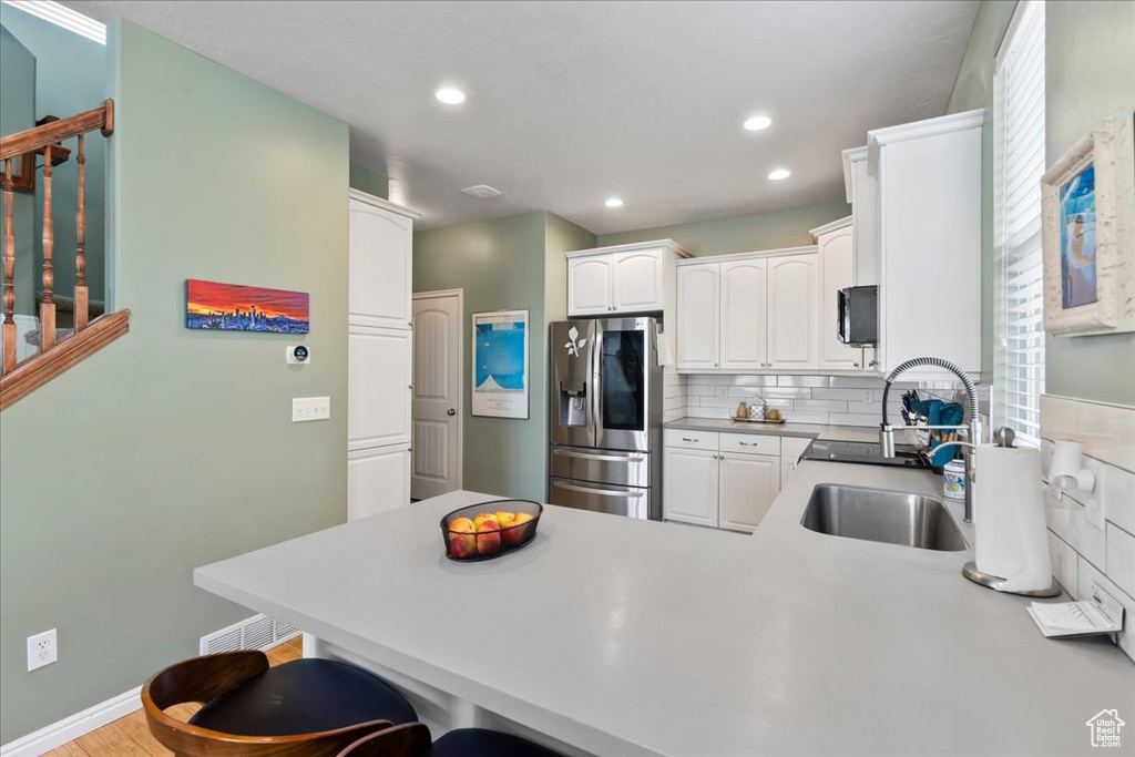 Kitchen with stainless steel fridge, a peninsula, a kitchen breakfast bar, white cabinets, and recessed lighting