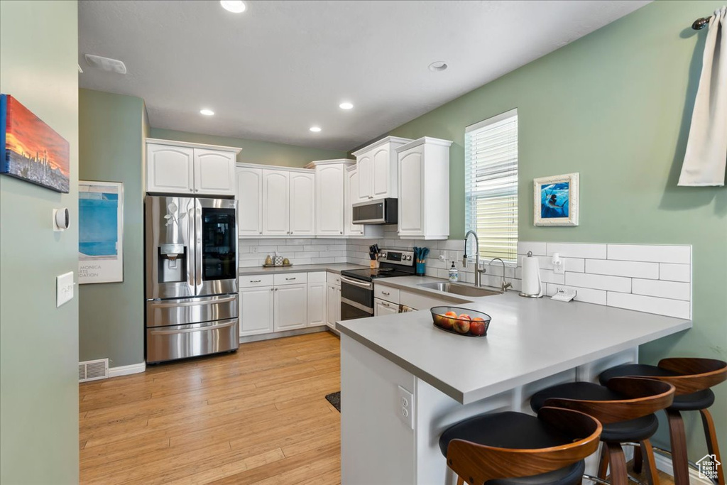 Kitchen featuring stainless steel appliances, a peninsula, backsplash, a breakfast bar area, and white cabinetry