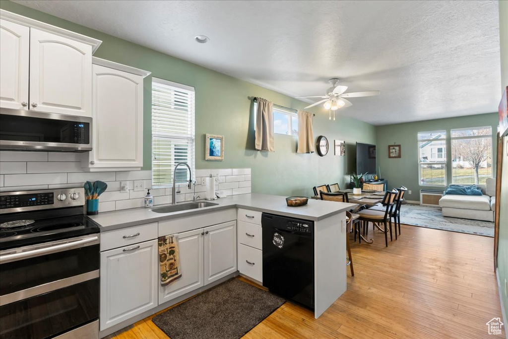 Kitchen featuring appliances with stainless steel finishes, a peninsula, a ceiling fan, tasteful backsplash, and white cabinets