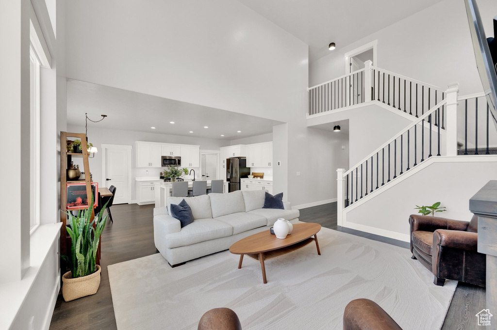 Living area with a high ceiling, dark wood-style floors, stairs, and recessed lighting