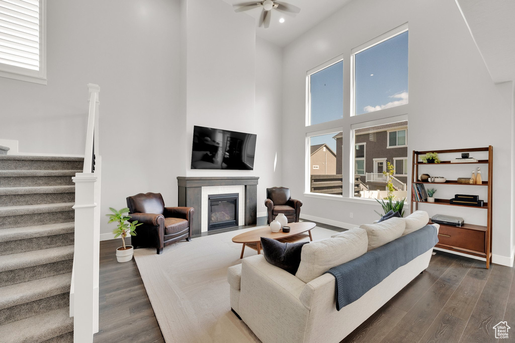 Living area with a high ceiling, stairway, ceiling fan, dark wood-type flooring, and a fireplace with flush hearth