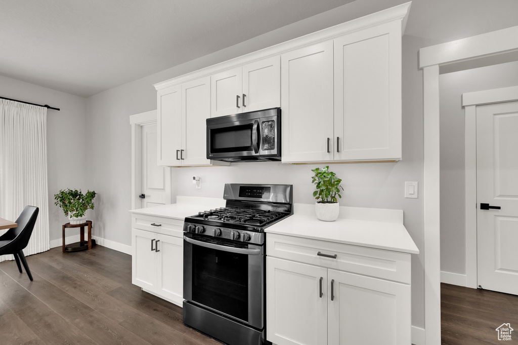 Kitchen with appliances with stainless steel finishes, light countertops, dark wood finished floors, and white cabinets