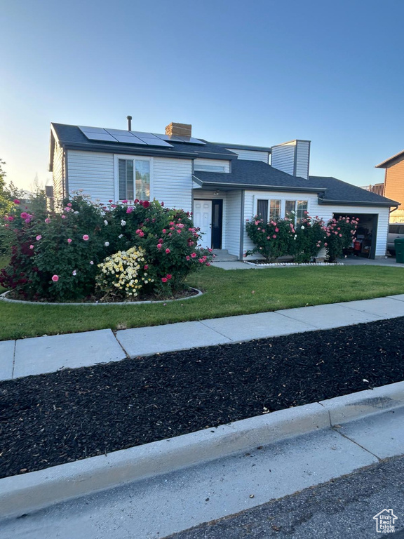 Traditional-style home featuring an attached garage, solar panels, a front lawn, and a chimney