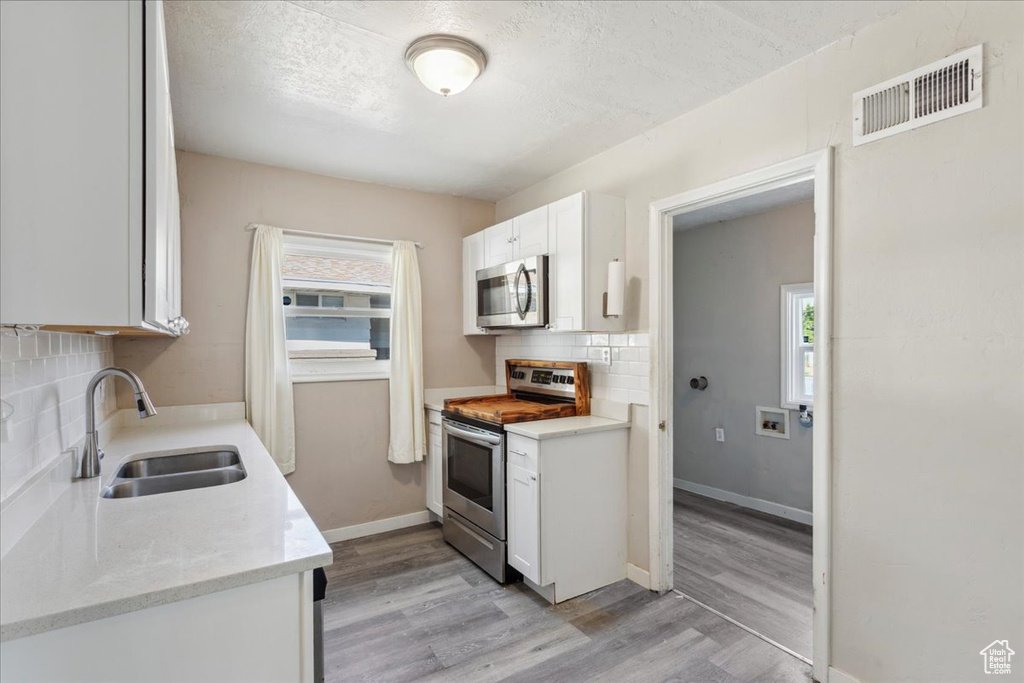 Kitchen with appliances with stainless steel finishes, backsplash, light wood-style flooring, white cabinetry, and a textured ceiling