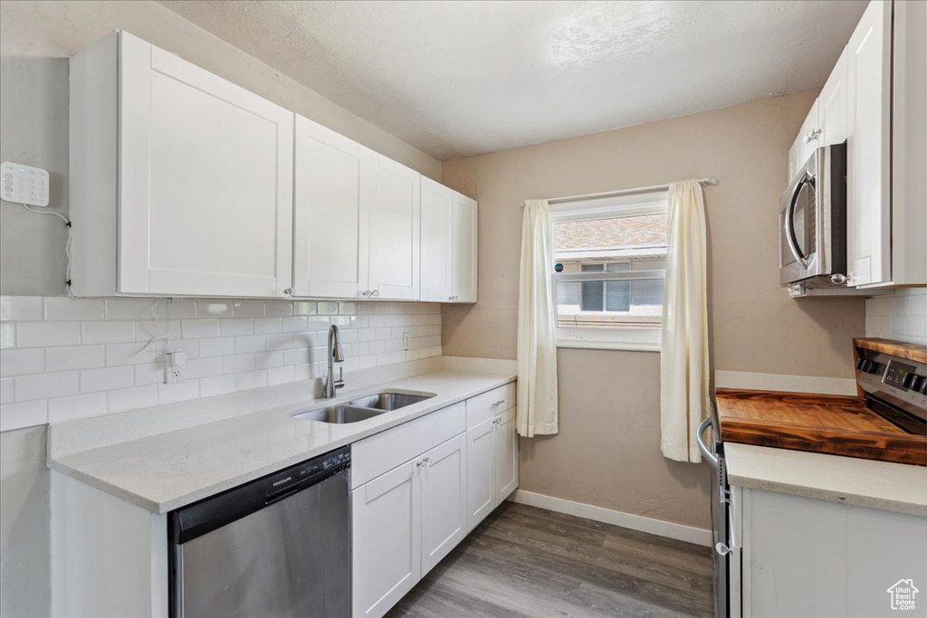 Kitchen with appliances with stainless steel finishes, wood finished floors, tasteful backsplash, and white cabinetry