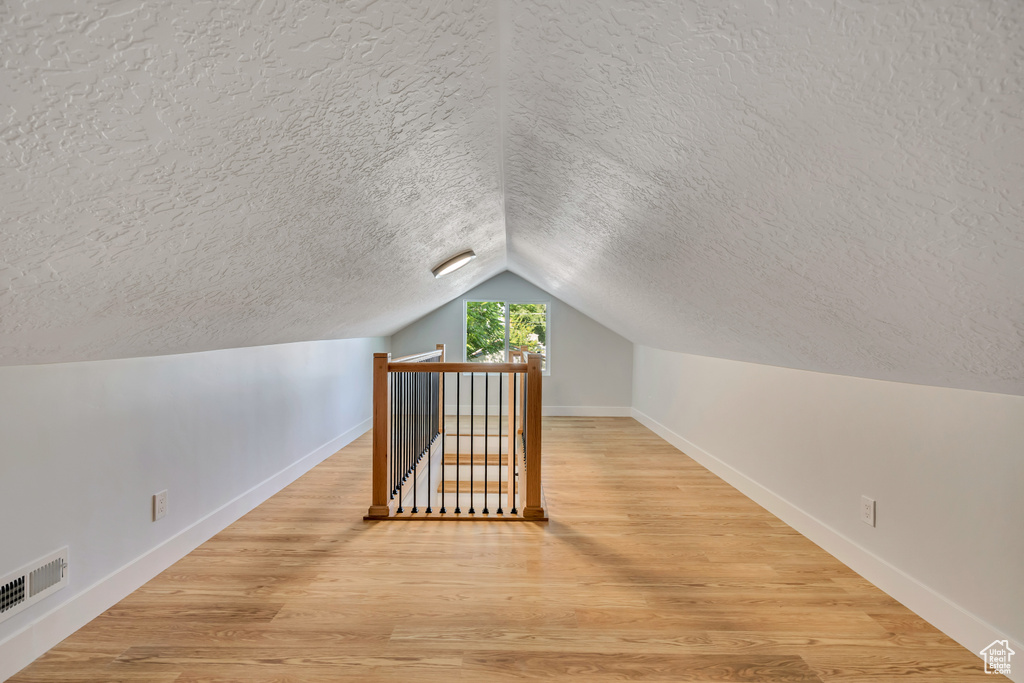Additional living space featuring a textured ceiling, lofted ceiling, and wood finished floors